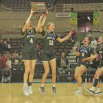 Caledonia seniors Josie Foster (#4) and Sienna Augedahl (#12) hoist the Section 1AA champions trophy while teammates rush in following the Warriors 63-53 win over Dover-Eyota. Caledonia’s girls are off to state. Photo by Paul Trende