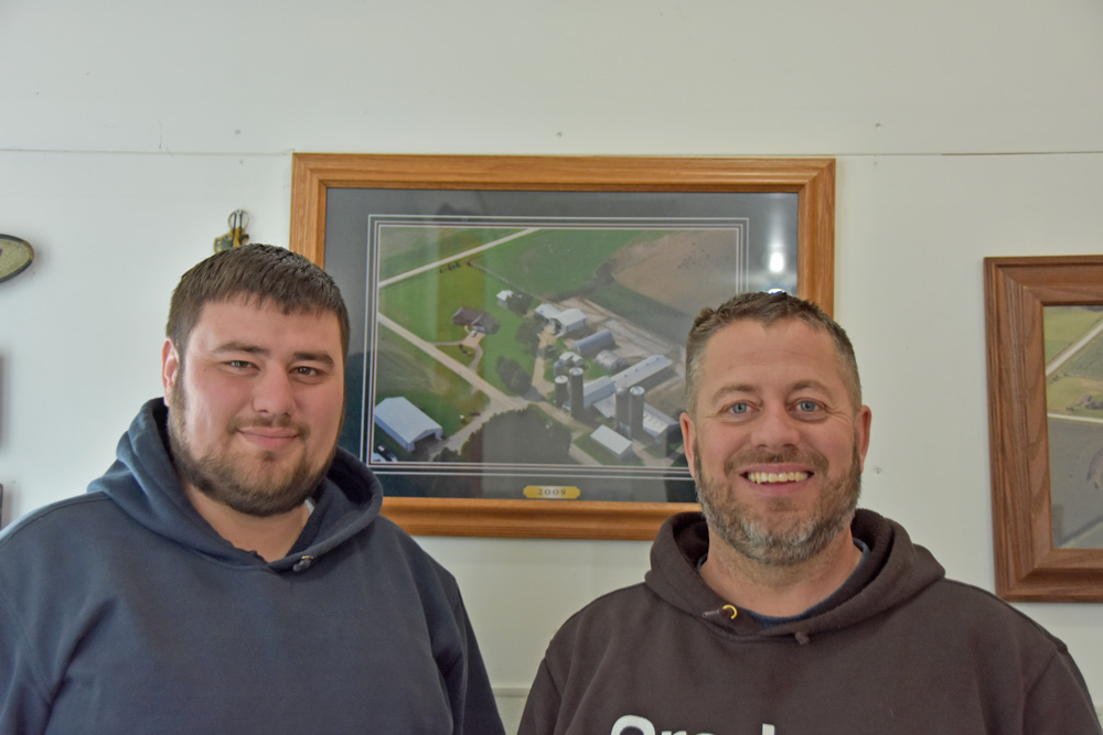 Cody and his dad Brian Erickson. Behind them is a photo of the family farm. Photo by Charlene Corson Selbee