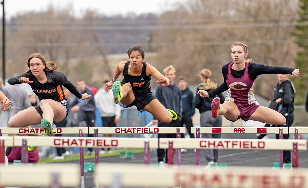 St. Charles’ Lydia Warmkagathe, LFCMC’s Ava Jacobsen, and Chatfield’s Rebecca Copeman clear the first hurdle near simultaneously at Chatfield’s home meet. Copeman won the 100-meter hurdle event. Photo by Leif Erickson