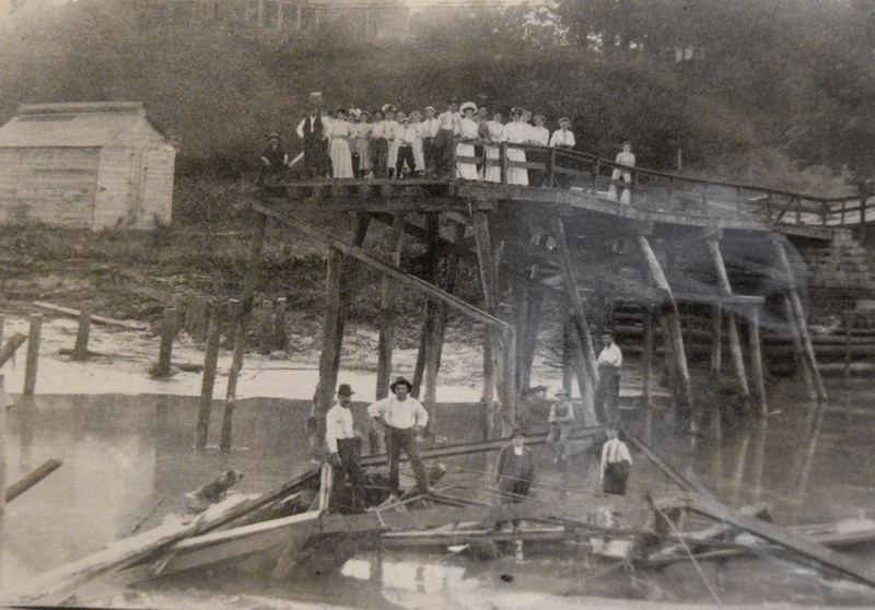 In August 1909, citizens of Hokah survey the damage, some standing in the lakebed and others atop the bridge that had spanned Lake Como just after a flood destroyed the bridge and the dam, thus draining the lake. The white building at left was an ice house. Photo courtesy of the Hokah Public Library