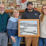 The Hazel family is holding a photo of the original Hazel family farm. From left to right, Brian, Judy, Adam and Maggie.