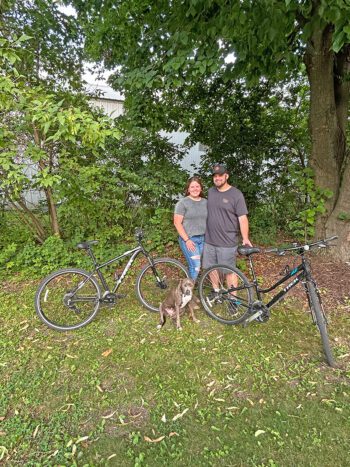 Carin Hyter and Josh Jacobson pose with their bikes and their team mascot, their dog Harlow. Photo by Wanda Hanson