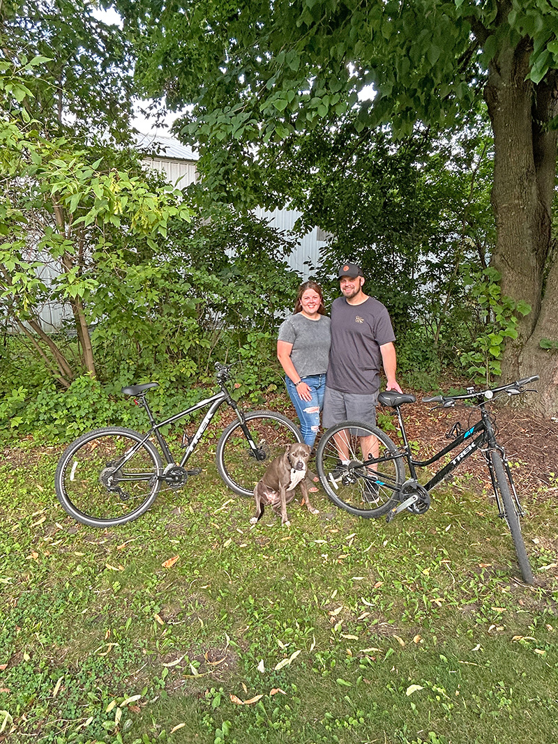 Carin Hyter and Josh Jacobson pose with their bikes and their team mascot, their dog Harlow. Photo by Wanda Hanson