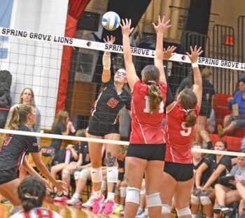 Spring Grove’s Madison Lile attacks over the outstretched arms of Houston defenders Jorja Meyer (left) and Taylor Stutzka (right) in the Lions’ 3-0 SEC sweep. Photo by Lee Epps