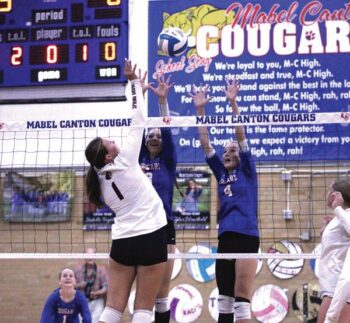 Spring Grove’s Brinley Middendorf challenges the Mabel-Canton double-block of Ella Halverson (left) and Braylee Stortz (right) in the team’s rivalry SEC match-up. The Cougars took the first two sets, but had to stave off SG’s comeback upset bid in five games (25-22, 25-17, 19-25, 19-25, 15-11), in the process continuing M-C’s 211 game SEC-match win streak. Photo by Paul Trende
