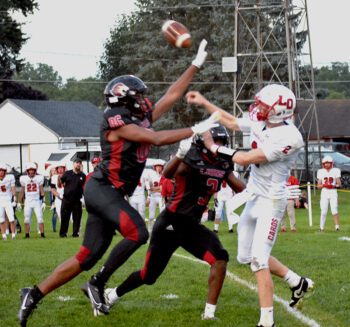 L-O/L/P quarterback Reid Hungerholt was pursued and pressured all night, here getting off a pass off over Spring Grove defenders (#86) Devon Williams and (#3) Ricardo Reynolds. Williams blocked both a punt and a pass while Reynolds had 12 tackles, five for loss, including a sack in the end zone for a safety in the Lions’ 37-12 win. Photo by Lee Epps