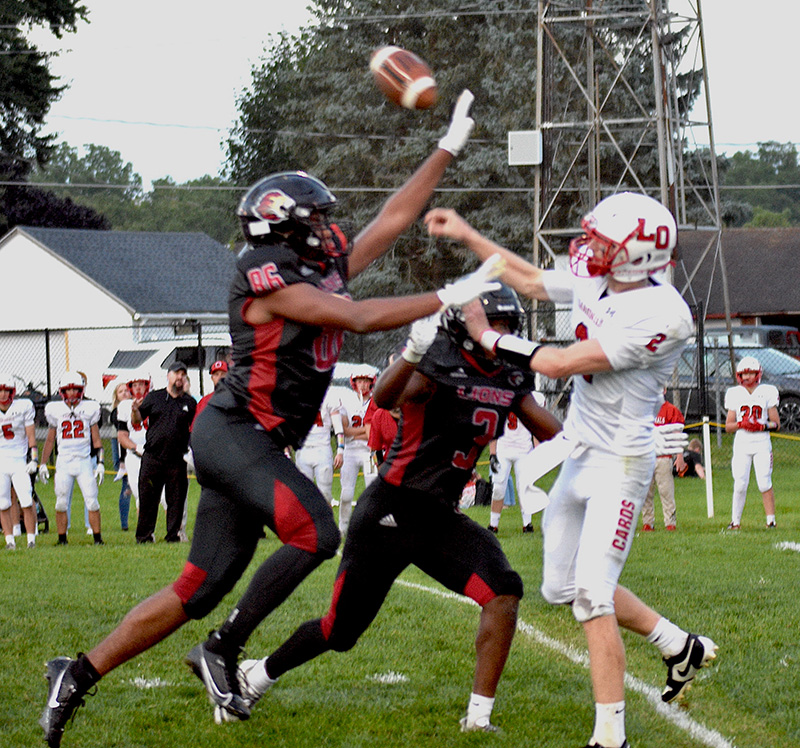 L-O/L/P quarterback Reid Hungerholt was pursued and pressured all night, here getting off a pass off over Spring Grove defenders (#86) Devon Williams and (#3) Ricardo Reynolds. Williams blocked both a punt and a pass while Reynolds had 12 tackles, five for loss, including a sack in the end zone for a safety in the Lions’ 37-12 win. Photo by Lee Epps