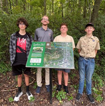 From left to right: Go Green member Isaak Michel, Mr. Jacob Kramer, Go Green Member Landan Betthauser and Mannix Darr. Isaak and Landan were involved in identifying the plants on the bluff along with five other Go Green members; Mannix is installing the trail marking signs and the kiosk for his Eagle Scout project. Photo by Wanda Hanson