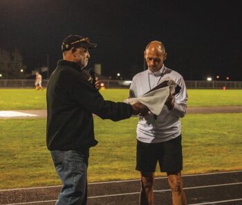 Roger Knutson delivers Caledonia head football coach Carl Fruechte a plaque after the Warriors beat Rochester-Lourdes 32-15. The victory was the 200th in Fruechte’s career, which notably includes 10 state football titles. Photo by Isaac Blocker