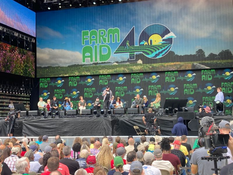 Farm Aid 40, September 20, 2025. Front row from left to right: Bonnie Haugen, Jim VanDerPol, Shorlette Ammons, Jennifer Fahy, Willie Nelson, Neil Young (speaking), John Mellencamp (sitting behind Neil Young), Dave Matthews, and Margo Price. Back row from left to right: Ruth Ann Karty, Kelsey Love Zaavedra, Angela Dawson, Moses Momanyl, and Hannah Bernhardt. Photo by Otto Wiegand
