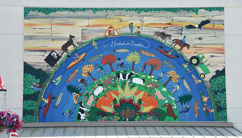 Hooked on Preston is located above the entrance to the city offices in downtown Preston. The mural, designed by former Preston resident Alison Love Unzelman, depicts life in Preston and the surrounding landscape. More than 500 community members, ranging in age from six months to 96 years, helped paint the aluminum panels. It was dedicated in 2017. Photo by Charlene Corson Selbee