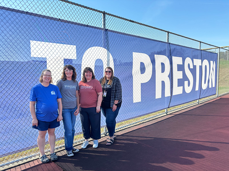 Preston EDA board member Alison Leathers, Preston Tourism Director Mandy Huston, Preston EDA Director Michelle Marotzke, and Gabby Kinneberg with the Minnesota Veterans Home - Preston, stood next to the banner. They were involved in the process of introducing this signage along with other signage throughout the city, which has been referenced as the Trout Route. Photo by Jason Sethre