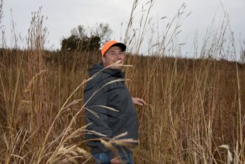 Craig Helke demonstrates how tall the native grasses get, which provide outstanding coverage for the pheasants during the winter. Photo by Charlene Corson Selbee