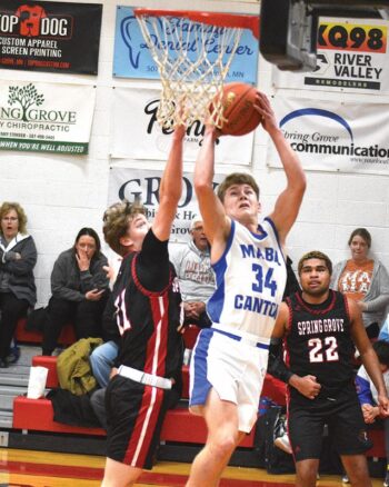 Spring Grove’s Kolton Nerstad challenges the shot of Mabel-Canton’s Kale Eiken. Getting some revenge from a couple football losses, the Lions topped the Cougars 72-59 in SEC action. Photo by Lee Epps