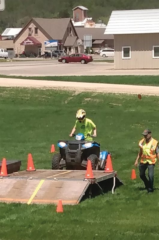 A student rides over a training ramp during Station 3 of an ATV safety course, demonstrating balance and control while a volunteer instructor walks alongside. Photo submitted
