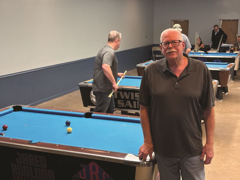 Jeff Knies stand next to one of the four pool tables set up in the Fountain Community Center in Fountain, Minn., during his annual three person tournament that draws top players from hundreds of miles. He’s been organizing this annual tournament, based out of Preston, Minn., for upwards of 35 years. Photo by Jason Sethre