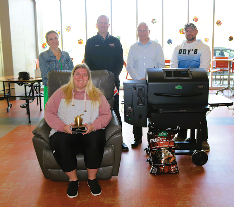 Teacher Courtney Graves sits in her new recliner from sponsor Drury’s Furniture with other prizes around her, and sponsors standing behind her. Photo by Barb Jeffers